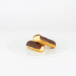 A single Lady M Chocolate Éclair sliced into half on top a white round plate.