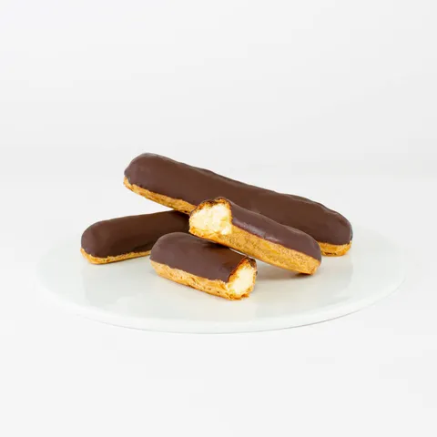 A Lady M Chocolate Éclair with one sliced into half on top a white round plate.