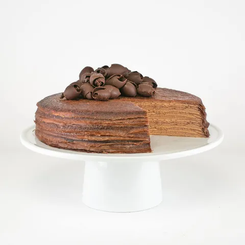 A sliced into Lady M Chocolate Mille Crêpes on top a white cake stand.