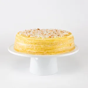 A whole Lady M Coconut Mille Crêpes cake sits on a white pedestal cake stand.