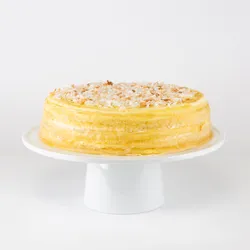 A whole Lady M Coconut Mille Crêpes cake sits on a white pedestal cake stand.