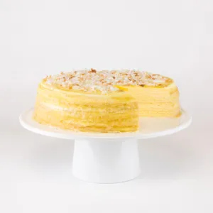 A whole Lady M Coconut Mille Crêpes cake on a white cake stand with one slice removed.