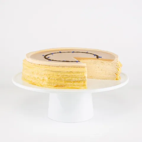 A sliced into Lady M Earl Grey Mille Crêpes on top a white cake stand.