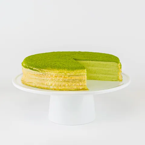 A sliced into Lady M Green Tea Mille Crêpes on top a white cake stand.