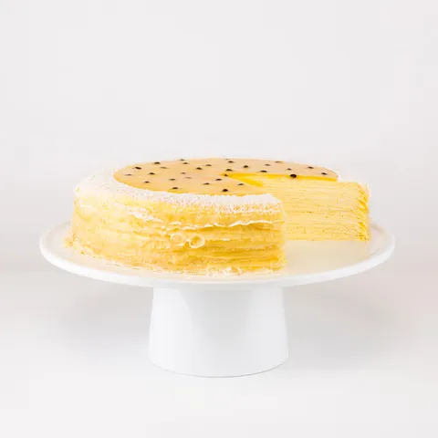 A sliced into Lady M Passion Fruit Mille Crêpes on top a white cake stand.