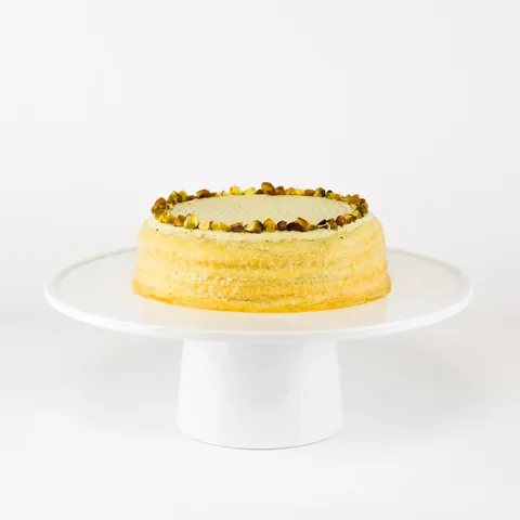 A 6-inch Lady M Pistachio Mille Crêpes on top a white cake stand.
