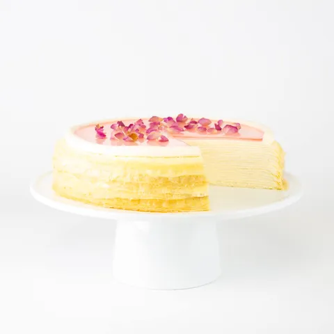 A sliced into Lady M Rose Mille Crêpes on top a white cake stand.