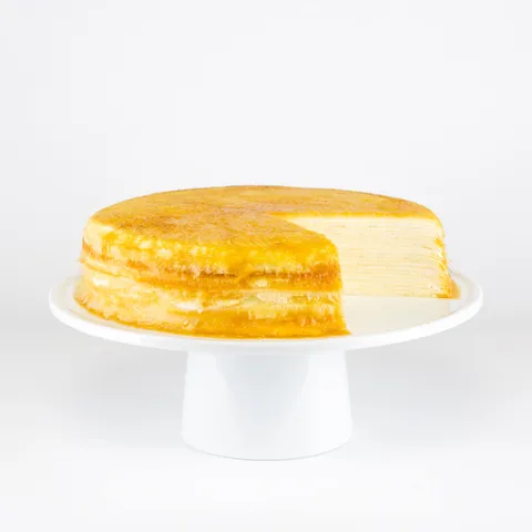 A sliced into Lady M Signature Mille Crêpes on top a white cake stand.