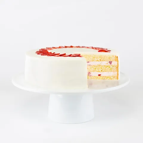A sliced into Lady M Strawberry Shortcake on top a white cake stand.