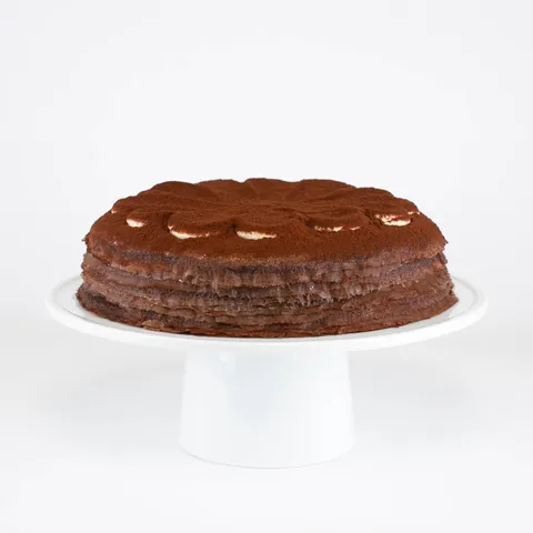 A Lady M Tiramisu Mille Crêpes on top a white cake stand.