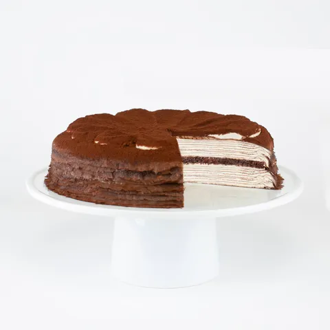 A sliced into Lady M Tiramisu Mille Crêpes on top a white cake stand.