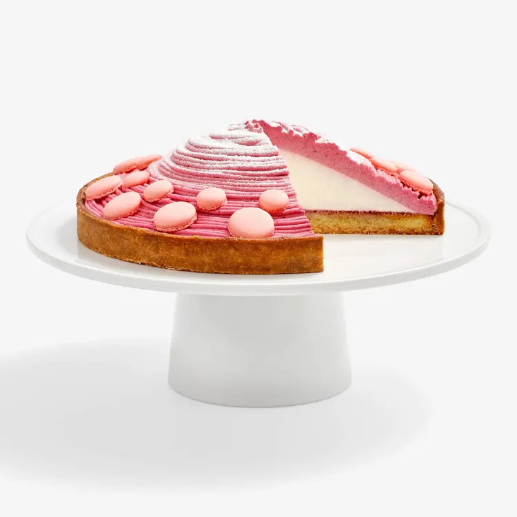Berry Mont Blanc Tart sliced into revealing the center layer of cream, a tart crust, and four-berry mousse. Topped with baby pink macaron shells and powdered sugar.