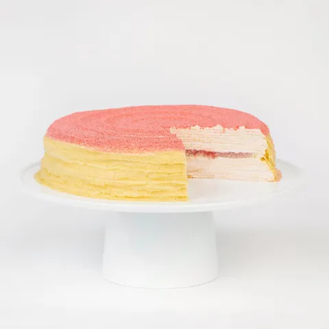 A thumbnail shot of a sliced into Lady M Strawberry Swirl Mille Crêpes on top a white cake stand.