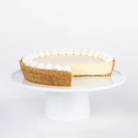 A thumbnail shot of a sliced into Lady M Coconut Cheesecake on top a white cake stand.