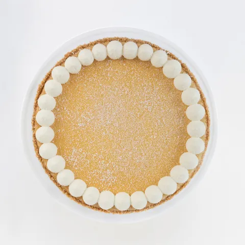 A top-down shot of a Lady M Coconut Cheesecake on top a white cake stand.
