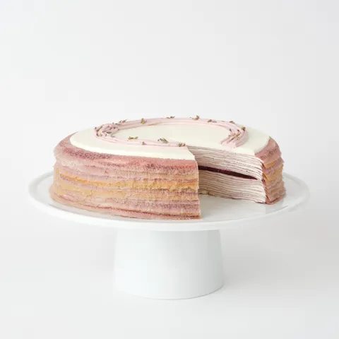 A thumbnail shot of a sliced into Lady M Lavender Mille Crêpes on top a white cake stand.