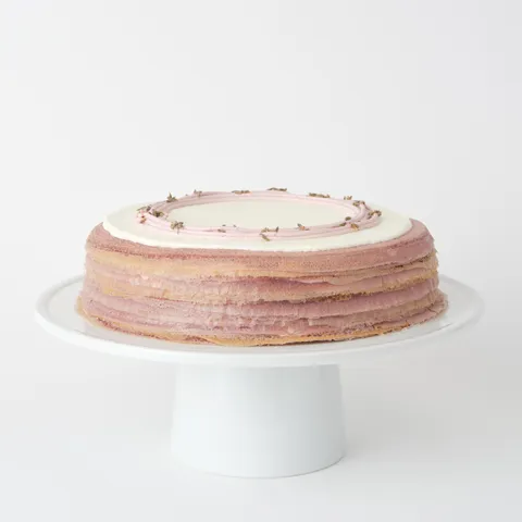 A thumbnail shot of a Lady M Lavender Mille Crêpes on top a white cake stand.