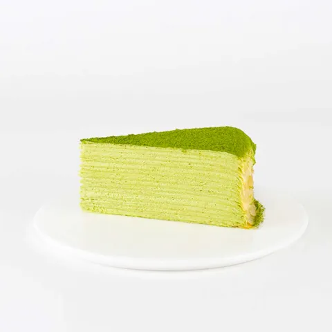 A thumbnail shot of a Lady M Green Tea Mille Crêpes slice on top a white round plate.