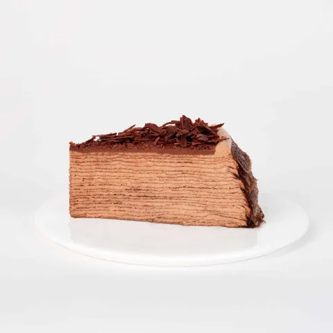 A thumbnail shot of a Lady M Amedei Chocolate Mille Crêpes slice on top of a white round plate.