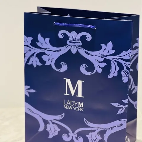 A thumbnail shot of a blue Lady M gift bag set over a marble table top.