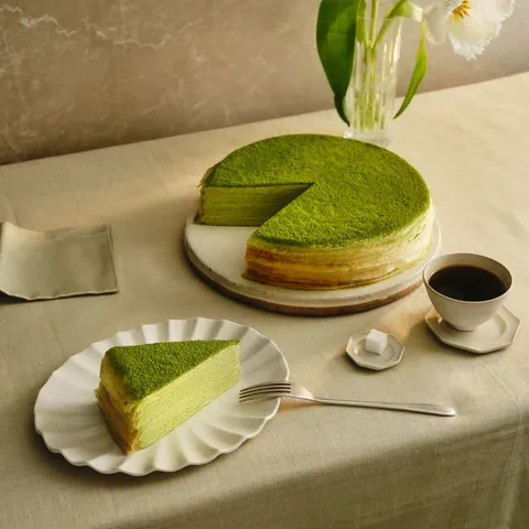A Lady M Green Tea Mille Crêpes with one slice served on a plate set over a beige linen.