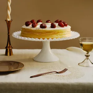 A Lady M Marron Mille Crêpes on top a white cake stand set on top a white linen.