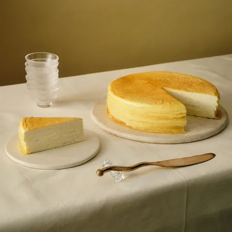 A Lady M Signature Mille Crêpes with one slice served on a plate over a white linen.