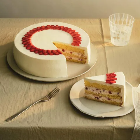 A Lady M Strawberry Shortcake with one slice served on a plate over a beige linen.