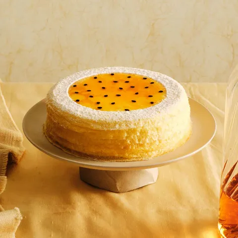 A whole Lady M Passion Fruit Mille Crêpes on top a round cake stand. Set over a yellow linen.