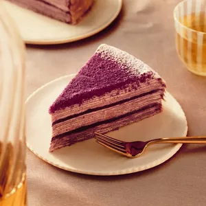 A slice of Lady M's Purple Yam Mille Crêpes on top a white plate set on a light-purple linen.