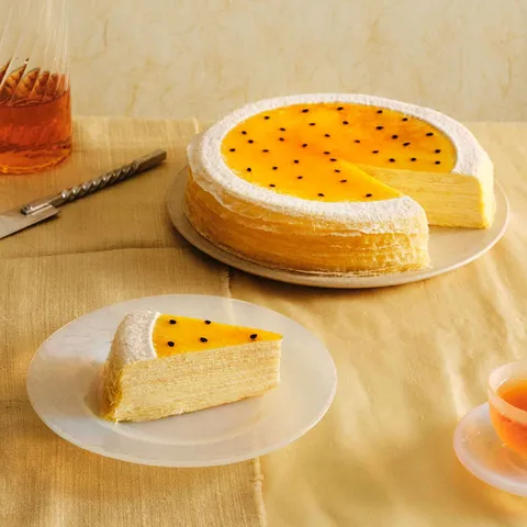 A Lady M Passion Fruit Mille Crêpes with one slice served on a plate, set on top a yellow linen.