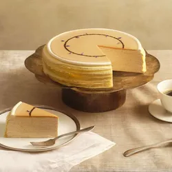 A Lady M Earl Grey Mille Crêpes with one slice served on a plate over a beige linen.