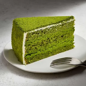 A slice of Lady M's Green Tea Mousse cake on top a white round plate set on a marble table.