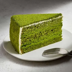 A slice of Lady M's Green Tea Mousse cake on top a white round plate set on a marble table.
