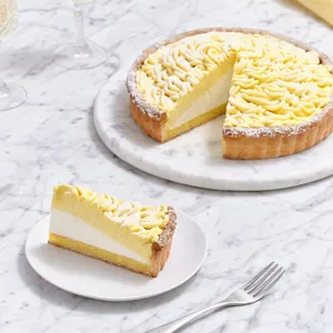 A Lady M Sweet Corn Tart with one slice served on a white plate over a marble table top.