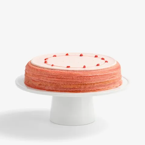 A thumbnail shot of a whole Lady M's Strawberry Matcha Mille Crêpes on top a white cake stand.