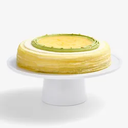 A whole Lady M's Yuzu Matcha Mille Crêpes sitting on top of a white round cake stand.