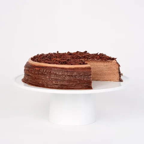 A Lady M Amedei Chocolate Mille Crêpes sliced into, sitting on top of a white round cake stand.