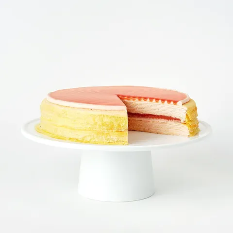 Guava Mille Crêpes cake with pink glaze and layers of guava cream, shown with a slice removed.