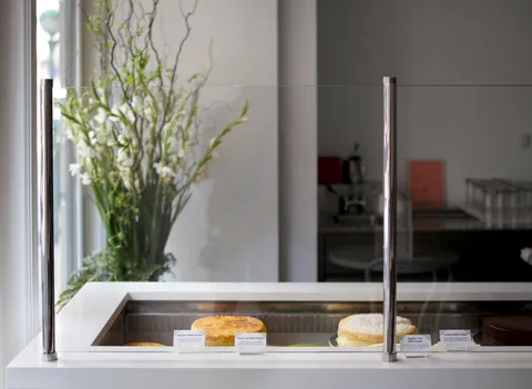 Lady M NoMad minimal cake display: whole cakes, cards, elegant green stems and white flowers behind.