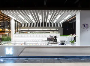 Modern white Lady M American Dream kiosk: slatted paneling, illuminated "M", colorful cakes, geometric lights, greenery, orchids.