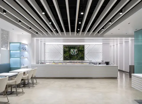 Lady M Sawtelle interior: long white cake display, floral "M" logo, black/white ceiling beams, small white tables.