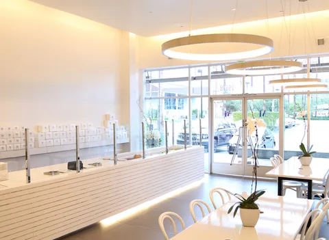 Lady M Irvine: white counter, cake display, circular lights, natural light, white tables/chairs, orchids. Sleek.