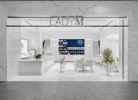 Lady M Tysons Galleria elegant storefront: marble exterior, "LADY M" logo, white interior, cake counter, blue display wall, white tables.