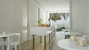 Lady M UES minimalist white interior: ribbed counter, small round tables, white chairs/teacups, pastries, 78th St view.
