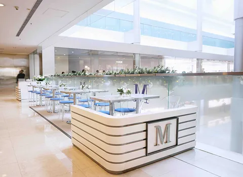Lady M Central IFC HK: white logo partition, glass dividers, blue seating, greenery, open, airy, natural light.
