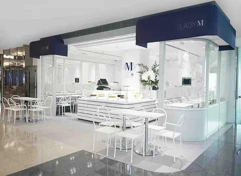 Lady M Kowloon Tong HK exterior: navy awning, white sign, glass walls. White striped counter, marble, logo, white furniture. Bright.