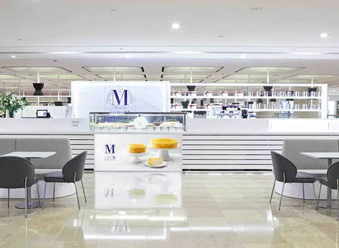 Lady M Admiralty HK: white striped counter with cake images, blue logo, display cases, gray tables, merch, flowers.