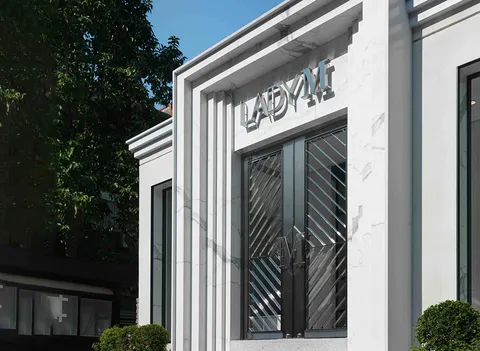 Lady M Taipei Flagship exterior: white marble, linear elements, geometric "M" handle doors, silver logo, blue sky.