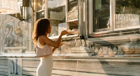 Guest in white dress orders cake at sunlit Lady M x Baccarat truck window.